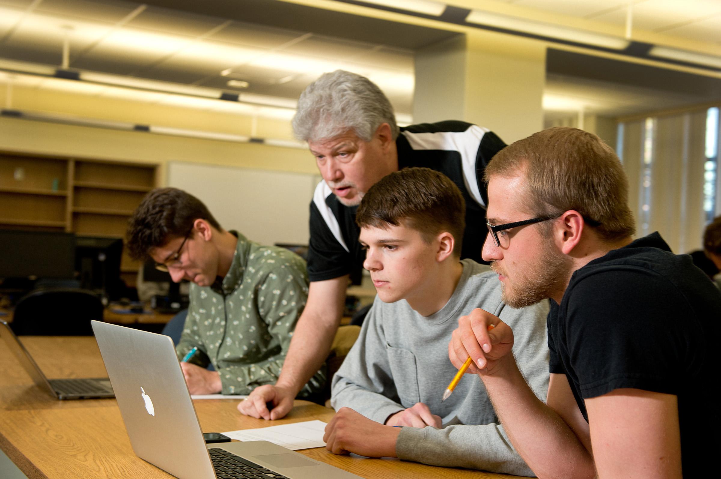 Professor teaching three students on their laptops